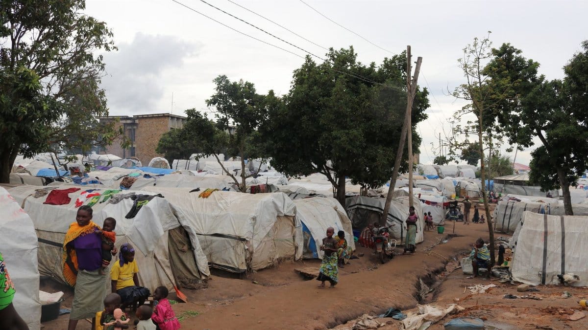 Overview of an African refugee camp with families and tents under trees, daytime