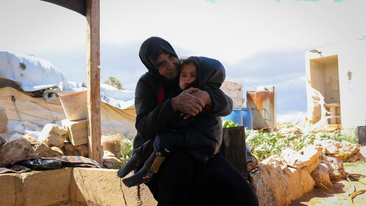 Mother and child embrace in a refugee camp in Idlib, Syria, amidst makeshift surroundings.