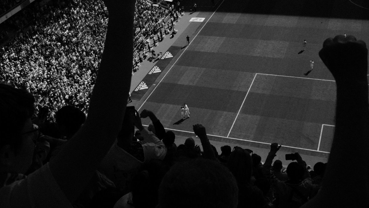 Fans cheering during a high-energy soccer match with players on the field, captured in black and white.