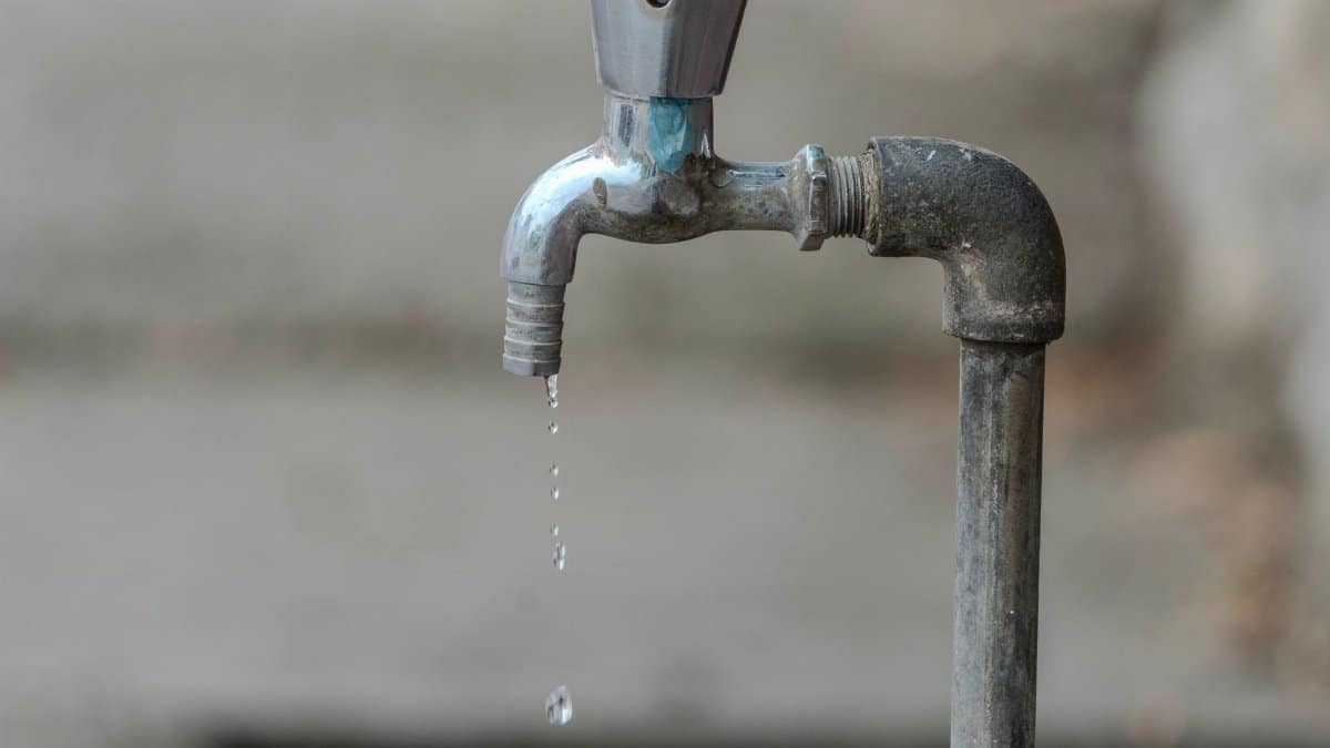 Close-up image of an outdoor water tap with a single droplet falling, highlighting water conservation.