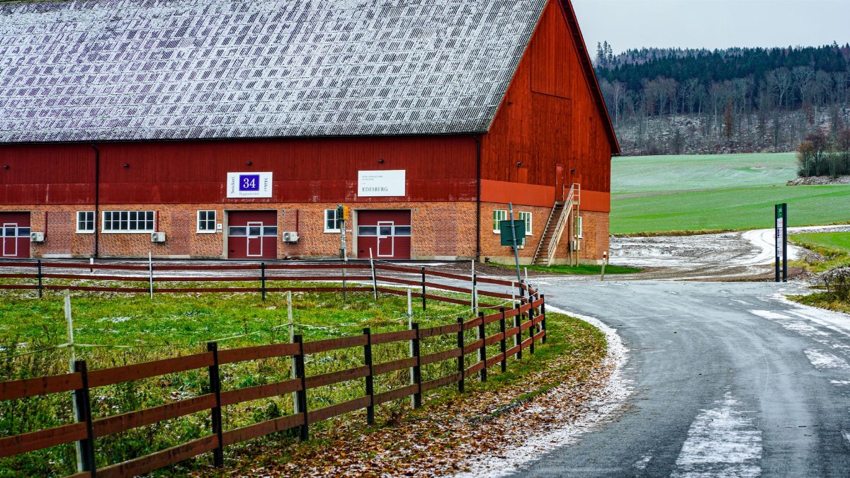 A picturesque red barn by a snowy road in a serene rural setting.