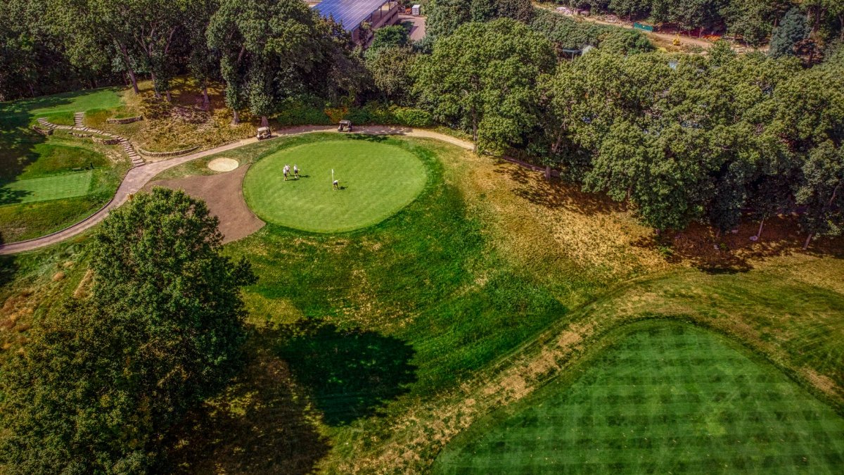 Aerial view of a lush golf course surrounded by trees, showcasing the vibrant greens under a sunny sky.
