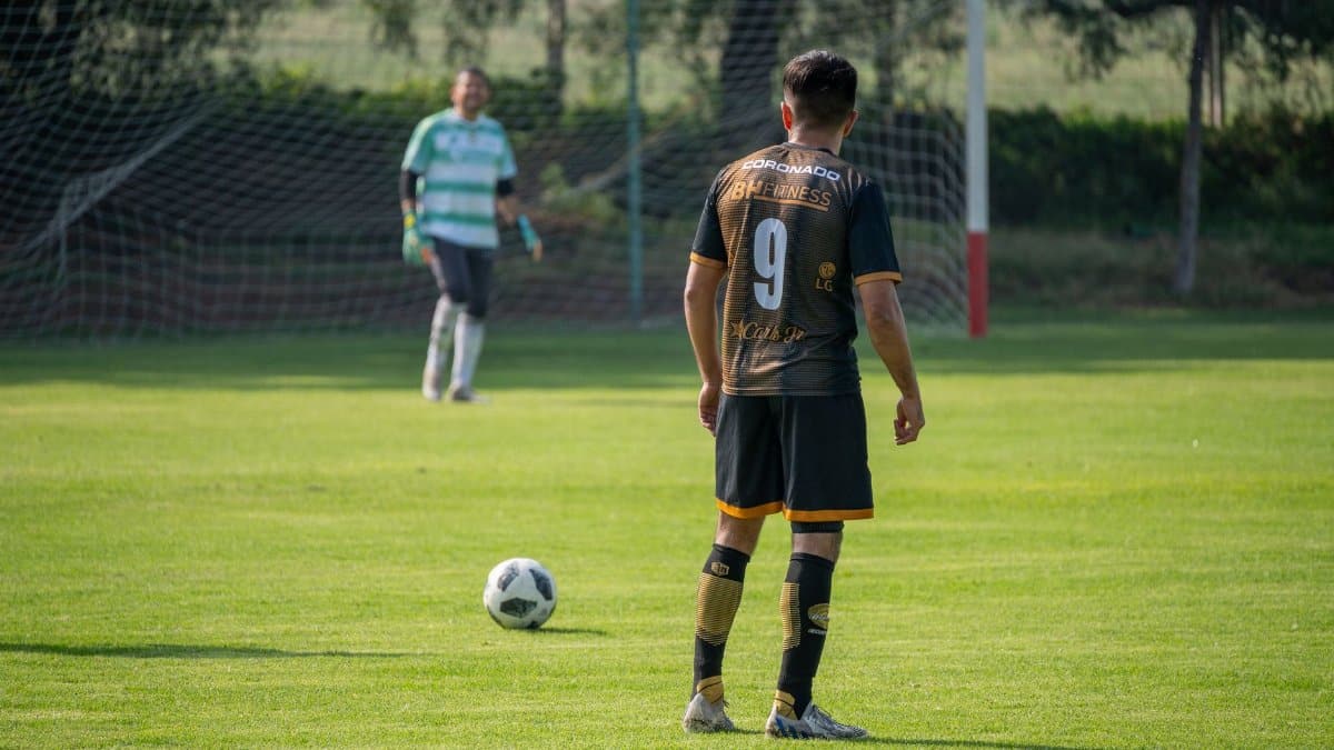 Soccer player in action preparing for a penalty kick on a sunny day in a green field.