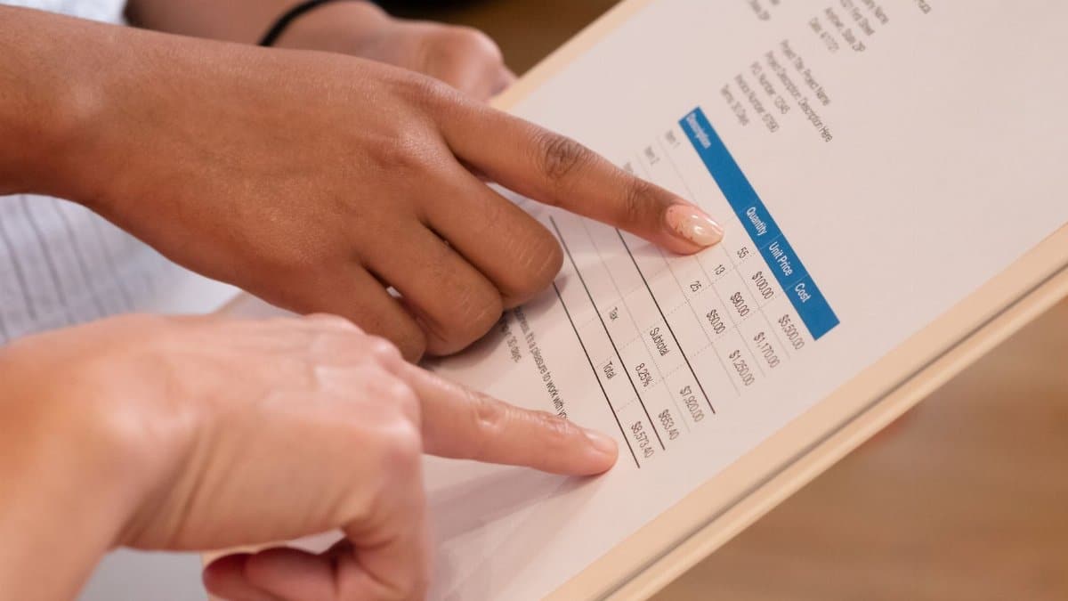 Two people pointing at financial details on a document, highlighting invoice analysis.