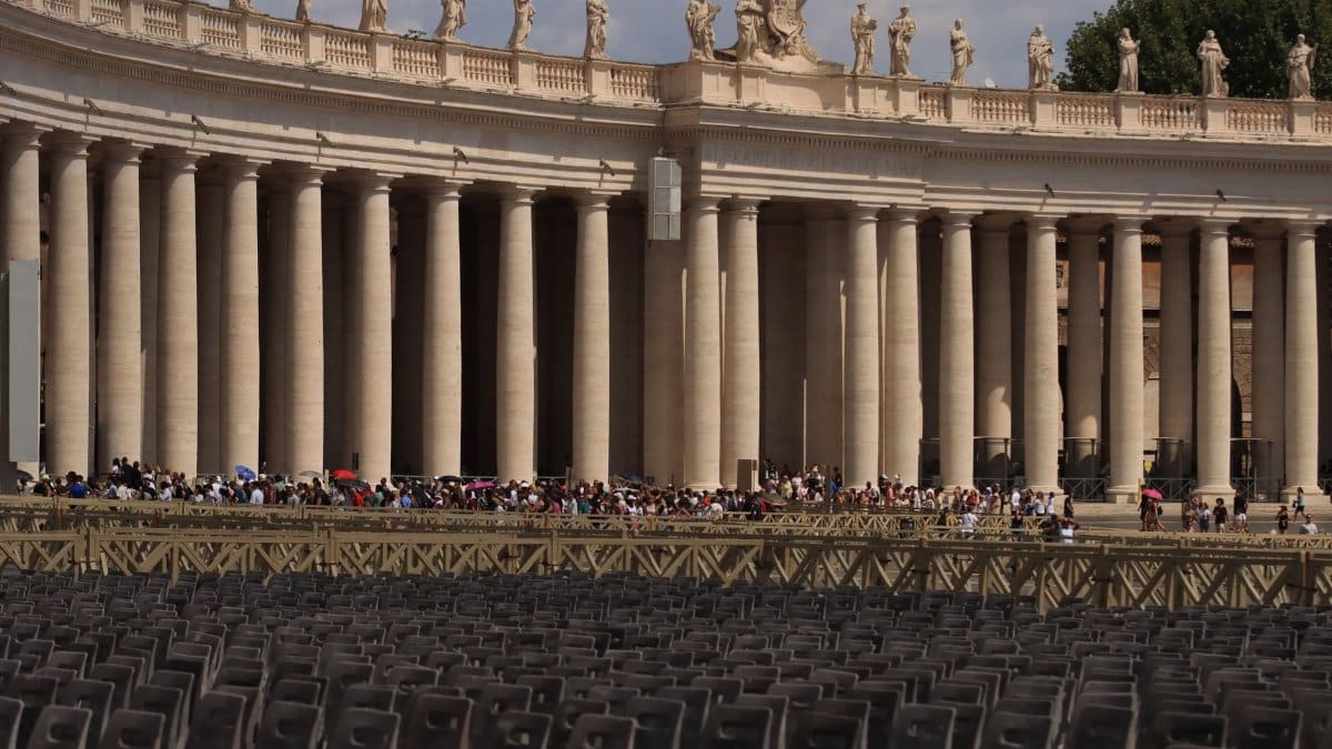 An iconic view of the colonnade in St. Peter's Square, Vatican City with a gathering crowd.
