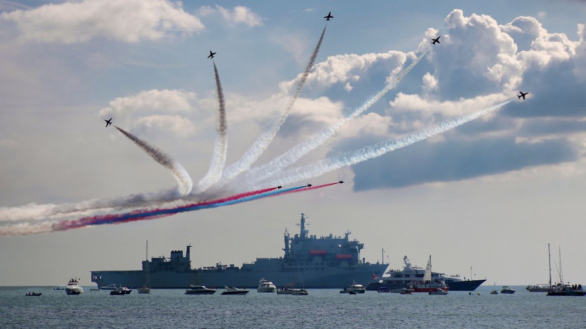 Stunning air display with colored smoke trails above naval ships on a sunny day at sea.
