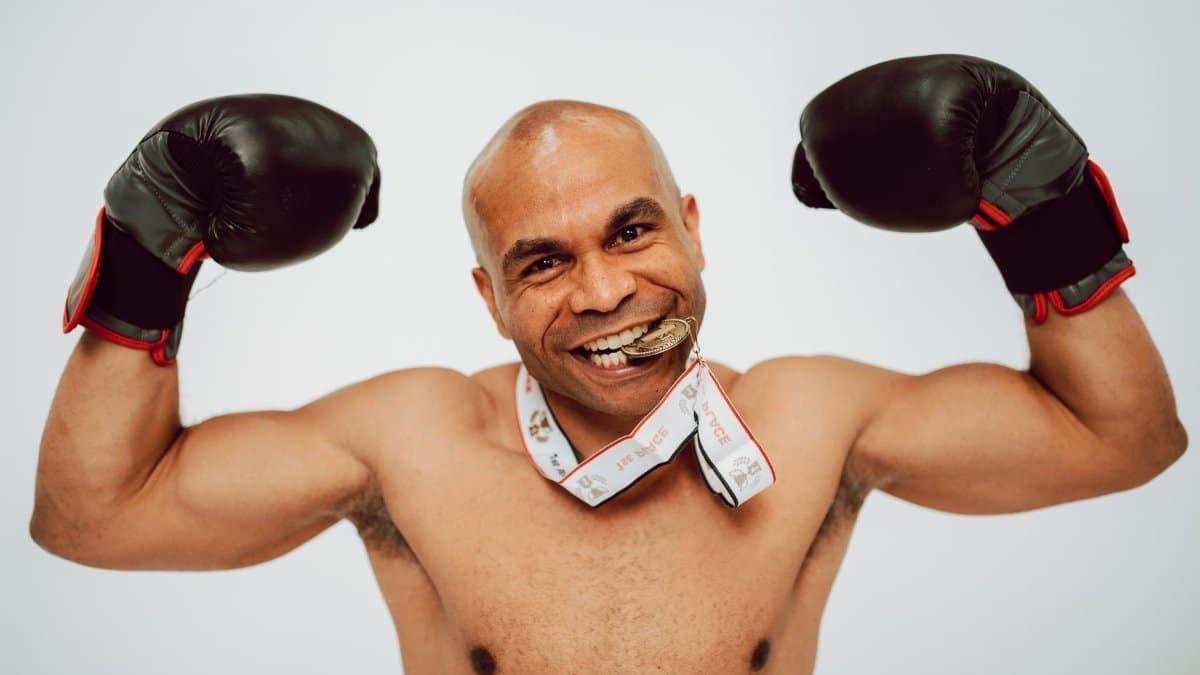 A victorious boxer poses confidently with boxing gloves and a medal in a studio setting.