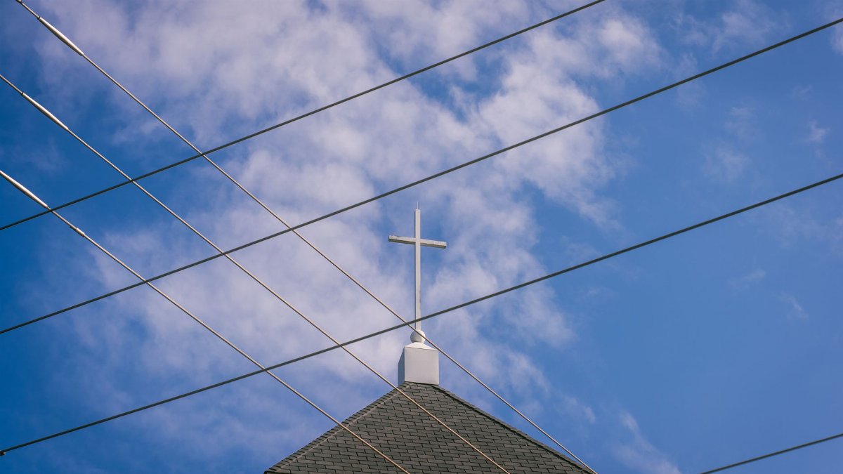 A church steeple with a cross set against a blue sky, intersected by power lines, creating an urban religious scene.
