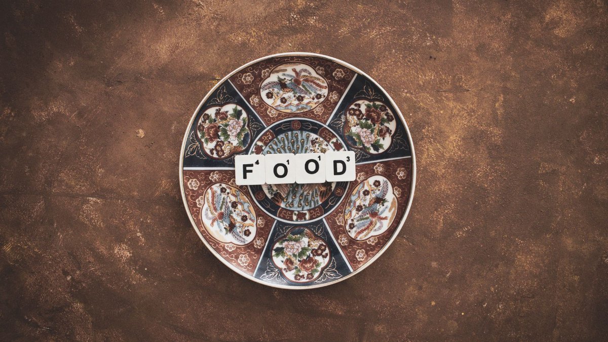 A decorative plate displaying the word 'FOOD' using Scrabble tiles on a textured brown surface.