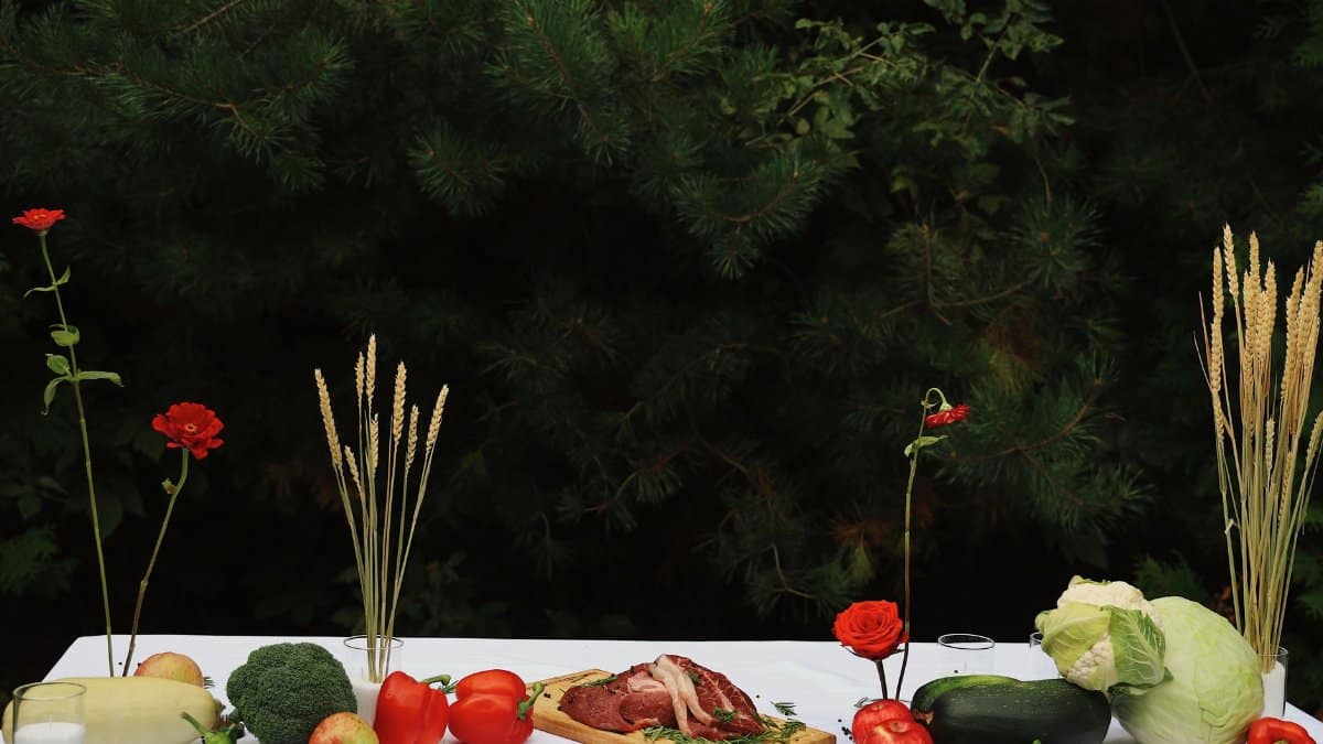 A rustic food table setup outdoors showcasing fresh vegetables and cuts of meat.