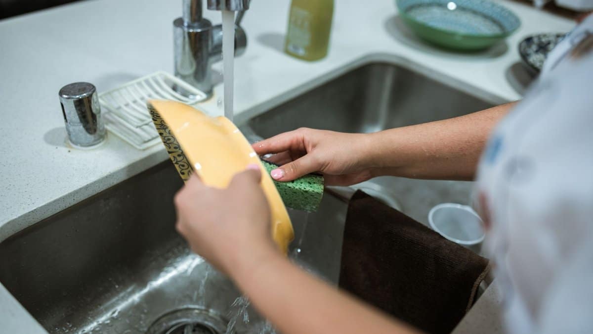 Close-up of hands washing dishes in a kitchen sink with running water.