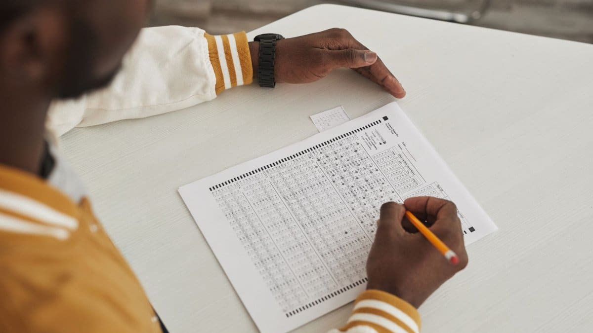 Focused student marking answers on a multiple choice exam sheet in a classroom setting.