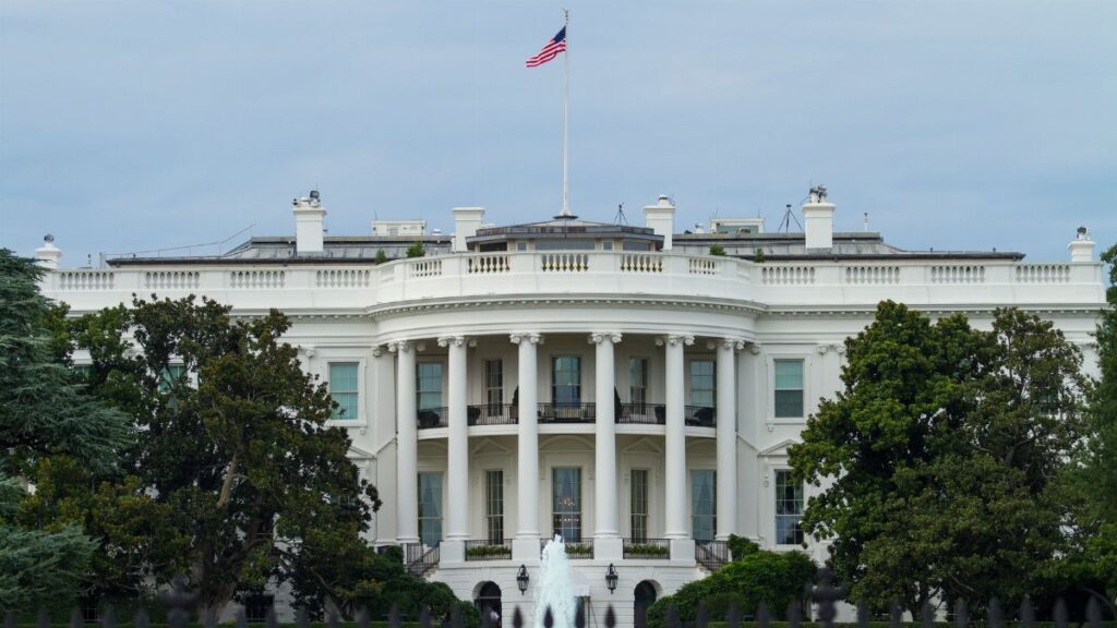 Front view of the iconic White House with the American flag, surrounded by greenery.