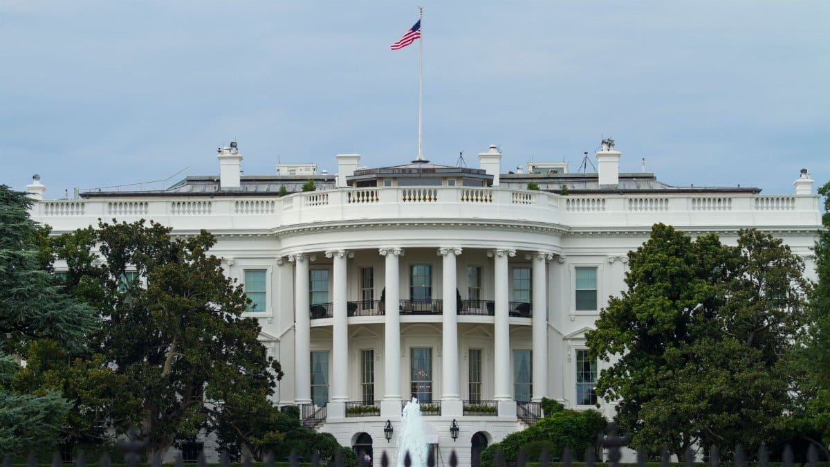 Front view of the iconic White House with the American flag, surrounded by greenery.