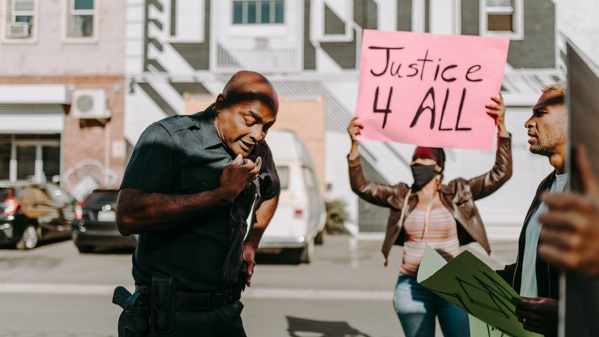 Protestors with signs engage with a police officer on an urban street.