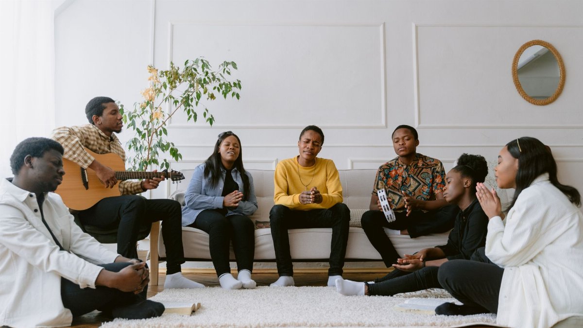 A diverse group of friends praying and singing together in a cozy living room setting.