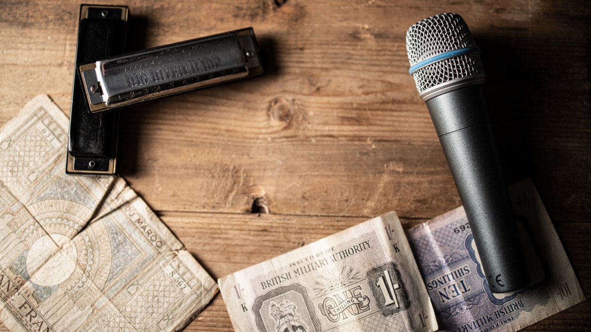 A microphone and harmonicas placed on rustic wooden surface with vintage currency.
