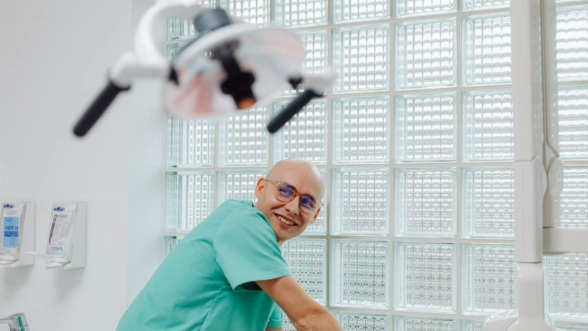Cheerful dentist in green scrubs smiling in a contemporary dental office.