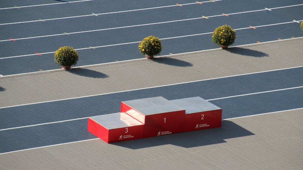 Red podium on a sunny outdoor athletics track with decorative plants.
