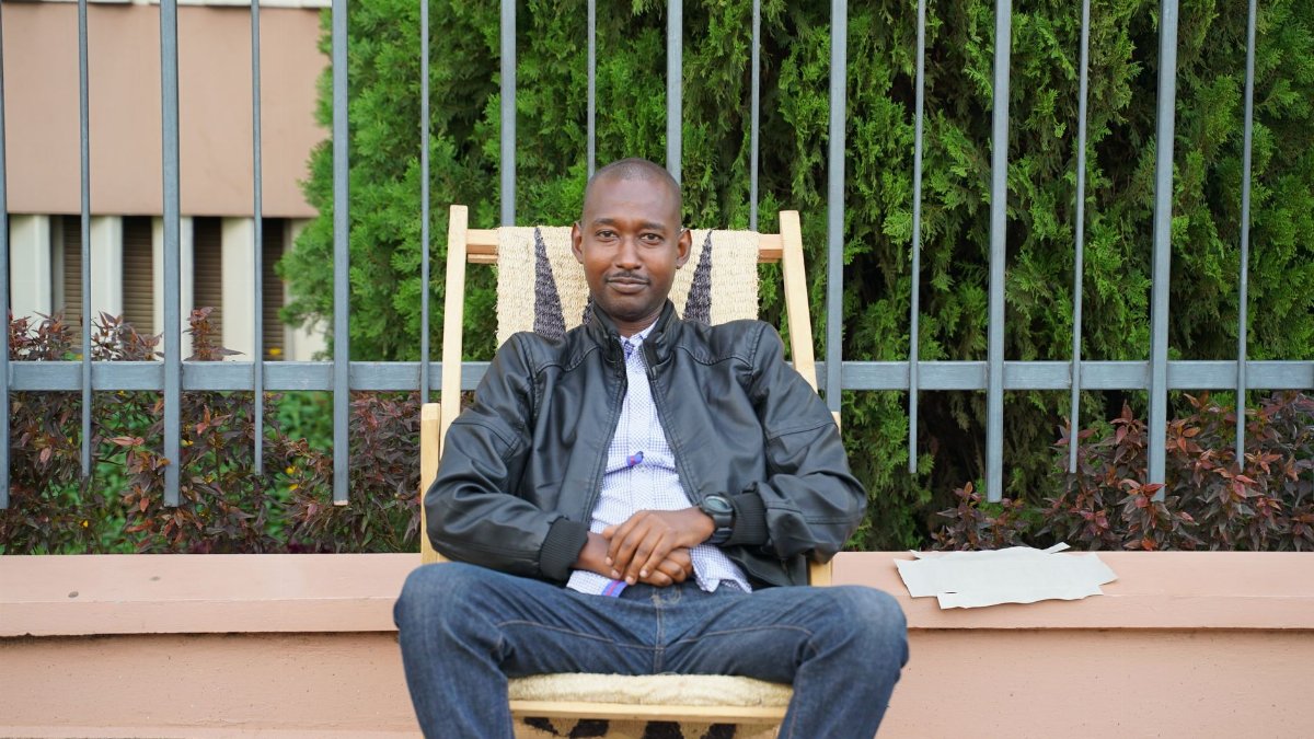 Man in leather jacket sitting on chair outdoors in Kigali, Rwanda.