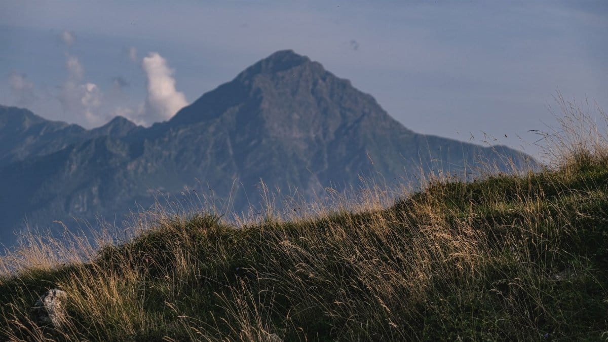A scenic view of a mountain range with lush grass under a blue sky.