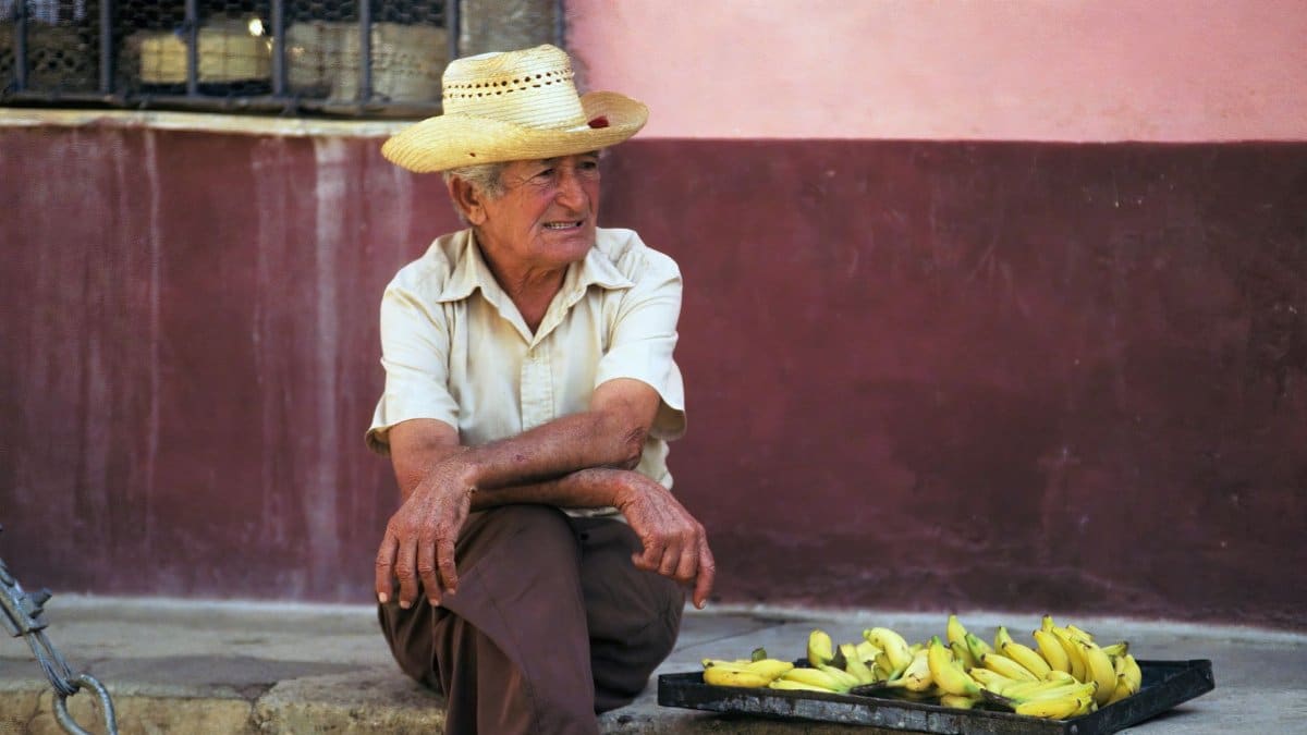 Elderly man in Cuba sitting with bananas on a sidewalk, showcasing local life.