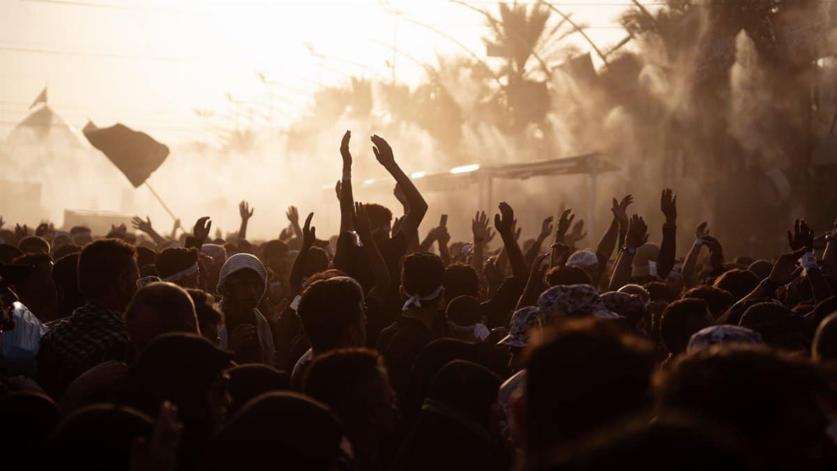 Silhouetted crowd raising hands during a sunset gathering in Karbala, Iraq.