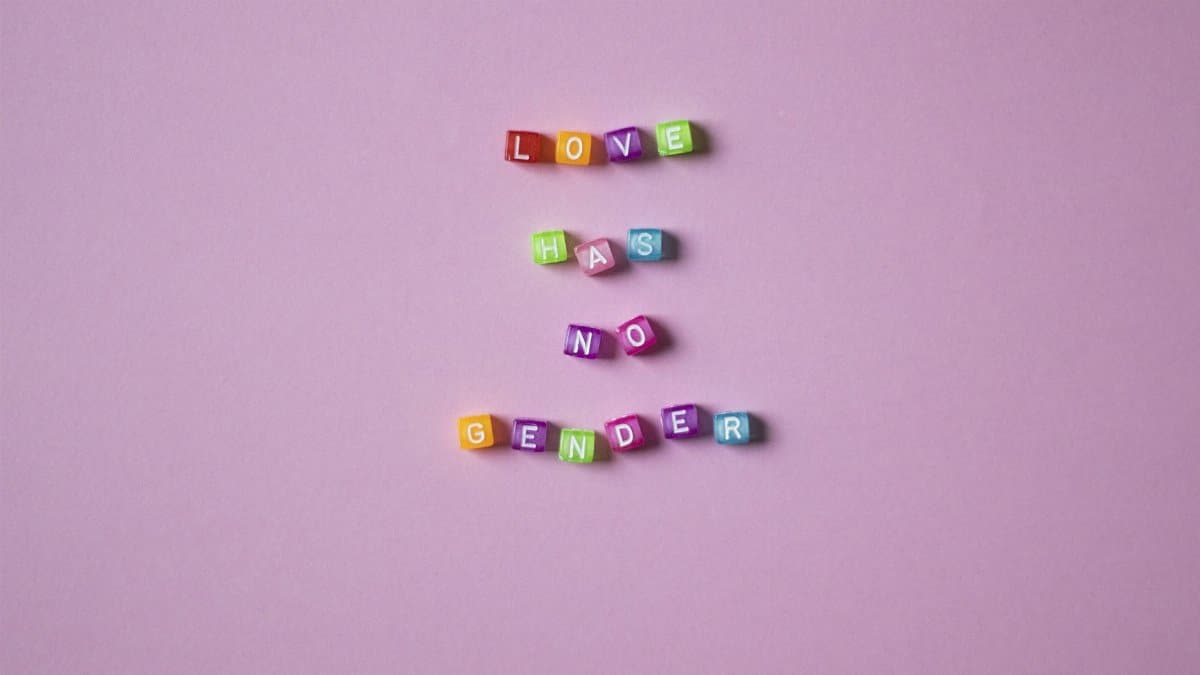 Colorful beads spelling 'Love Has No Gender' on a pink background, emphasizing inclusivity.