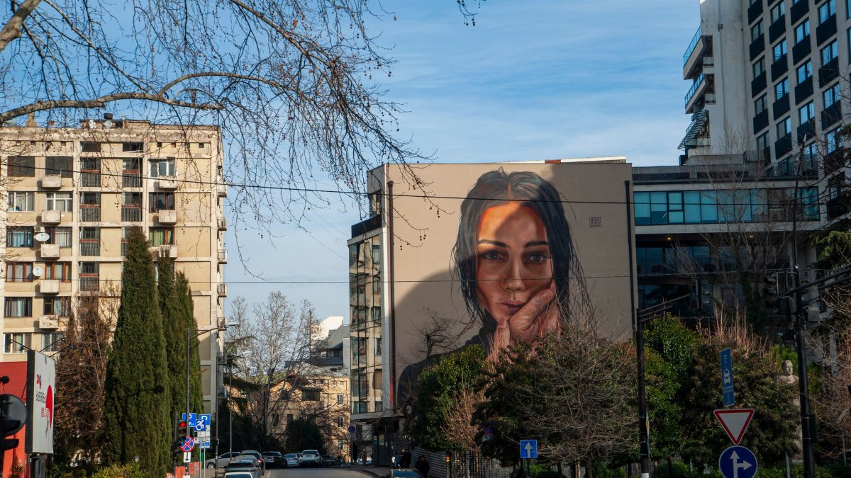 Striking mural depicting a woman's face adorns a building in Tbilisi, Georgia, blending art and city life.