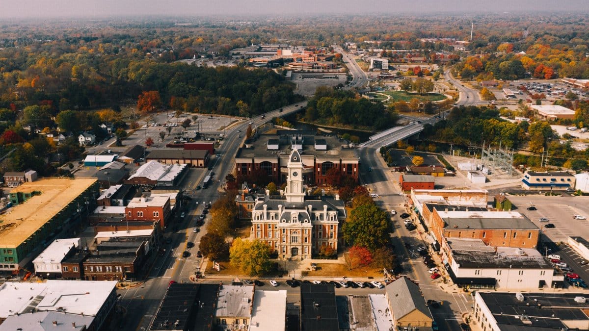 Drone view of aged stone building facades near urban roadways and bright trees in town in fall