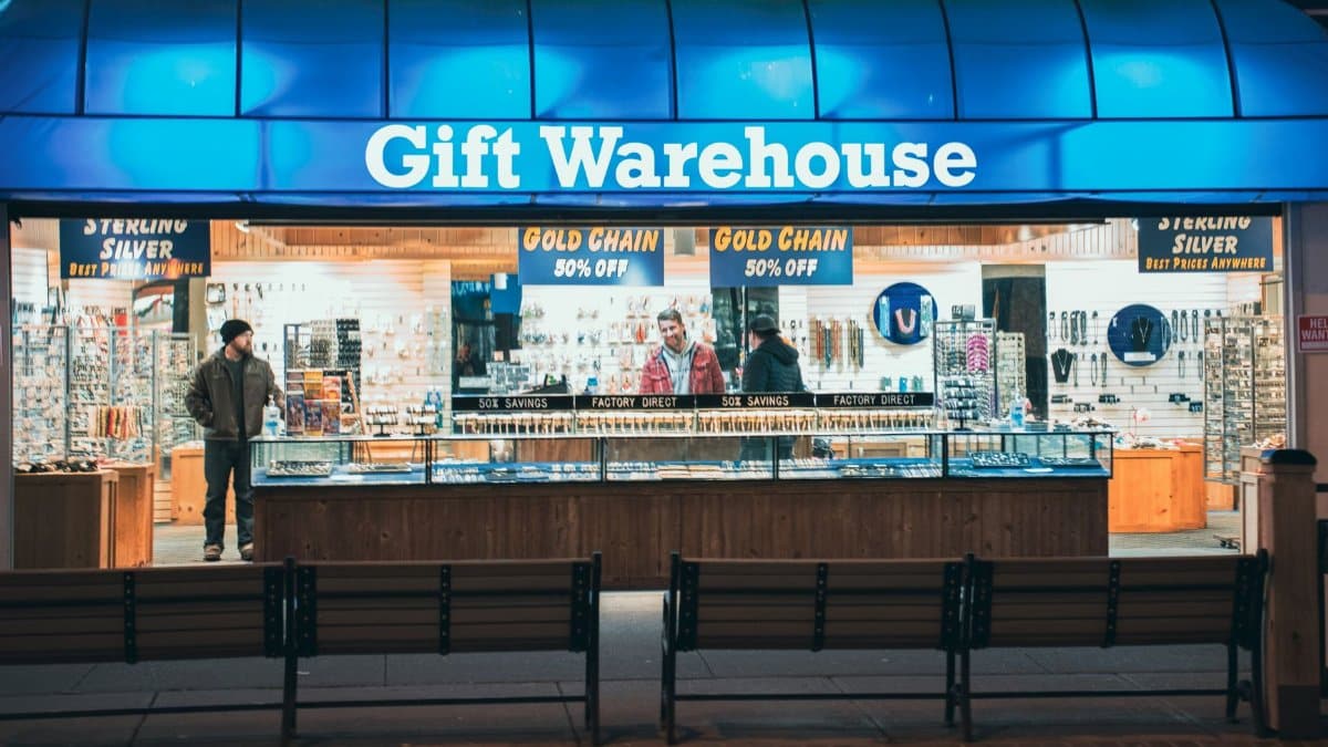 Night view of Gift Warehouse store with vibrant blue signage and two people inside.