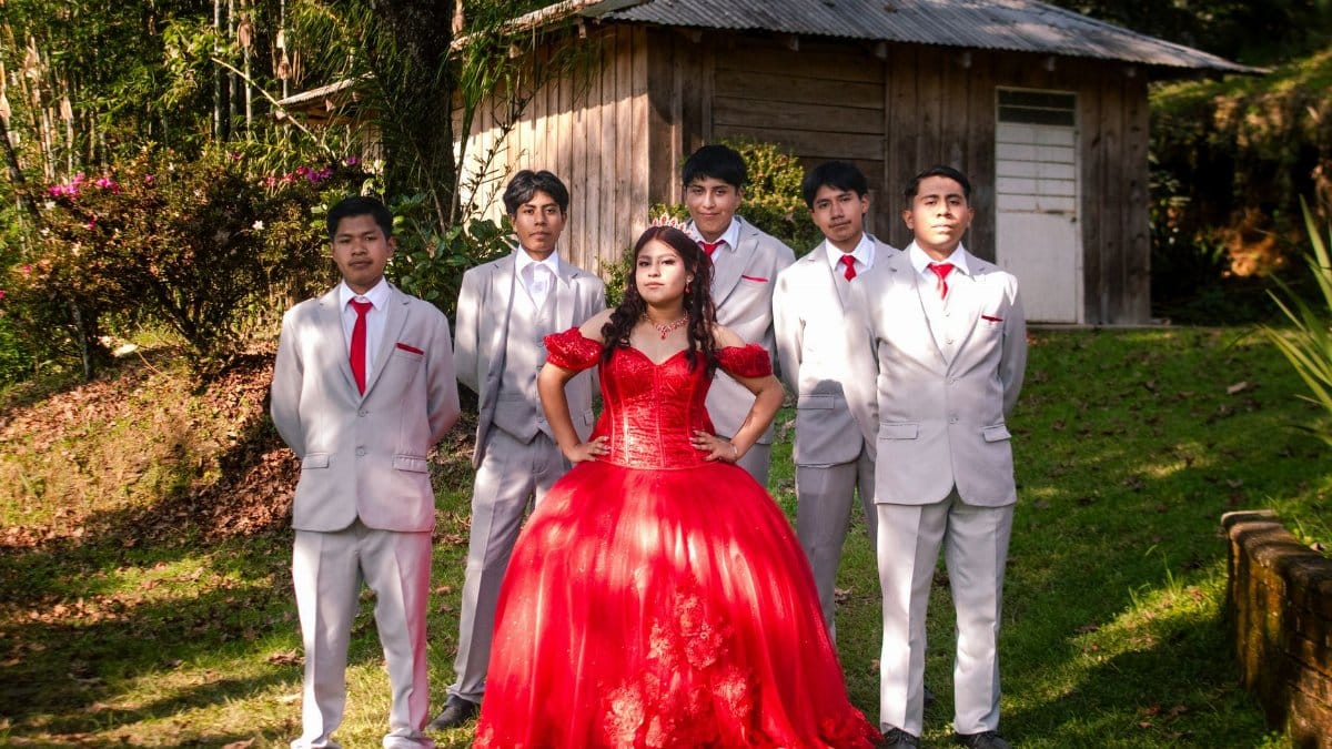 A proud quinceañera in a red gown poses with young men in suits, capturing a special milestone celebration outdoors.