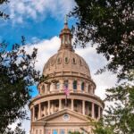 View of the iconic Texas State Capitol dome framed by lush trees under a vibrant sky in Austin, TX.