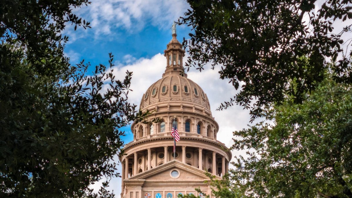 View of the iconic Texas State Capitol dome framed by lush trees under a vibrant sky in Austin, TX.