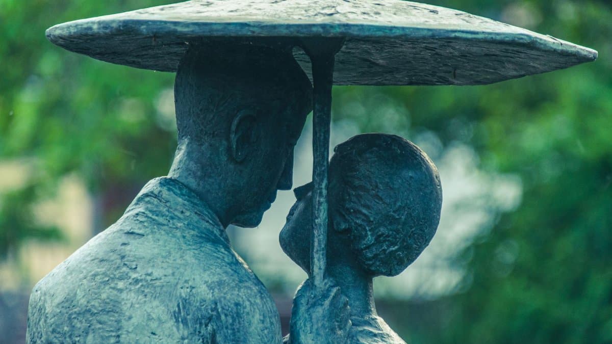 Close-up of a romantic bronze sculpture couple under an umbrella, evoking intimacy and art.