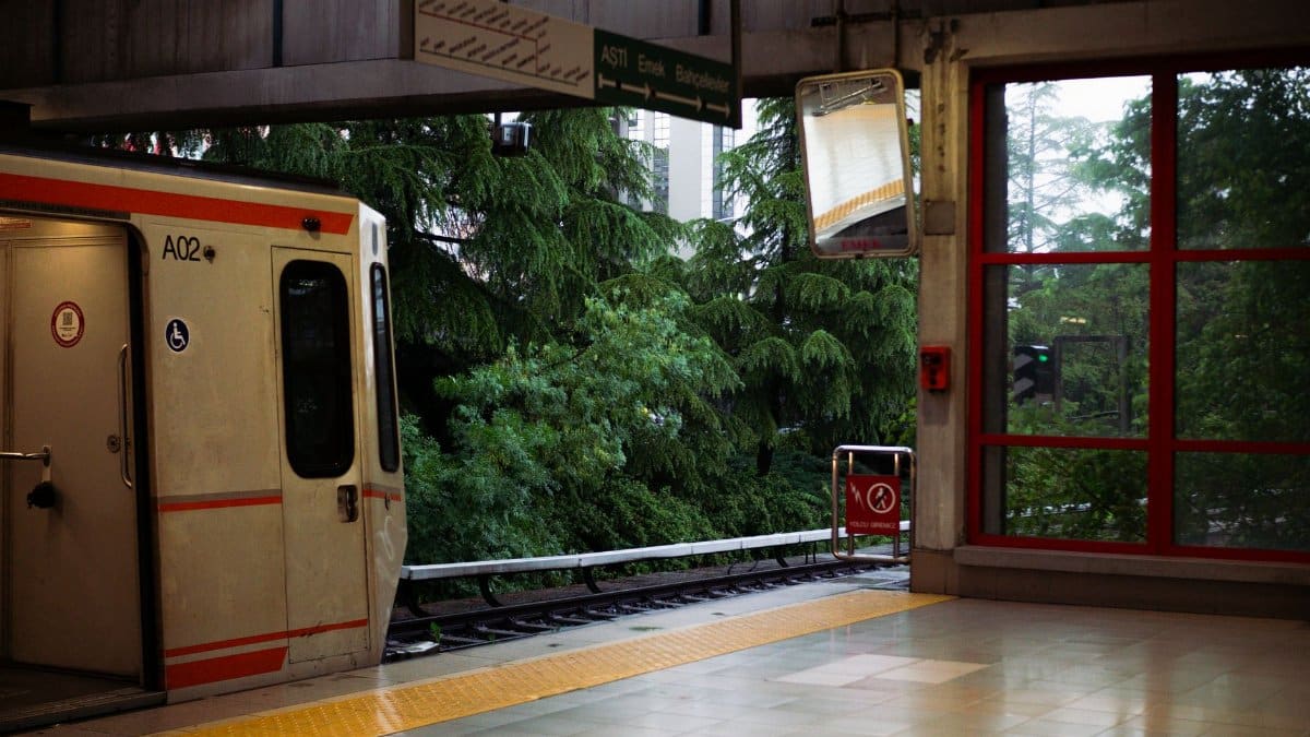 An empty metro platform with a train in Ankara, Türkiye, surrounded by lush green foliage.
