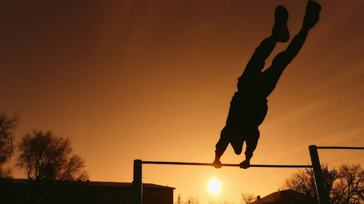 A silhouetted athlete performs on a pull-up bar against a vibrant sunset sky.