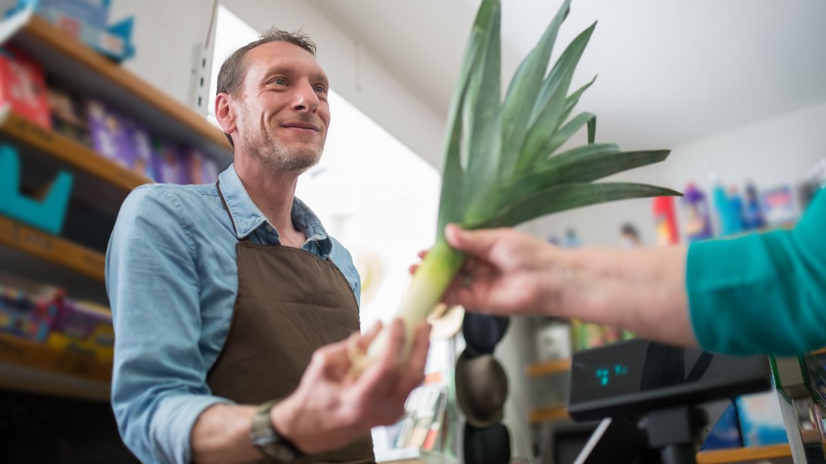 Friendly clerk assisting in vegetable purchase at a grocery store, showcasing personal customer service.