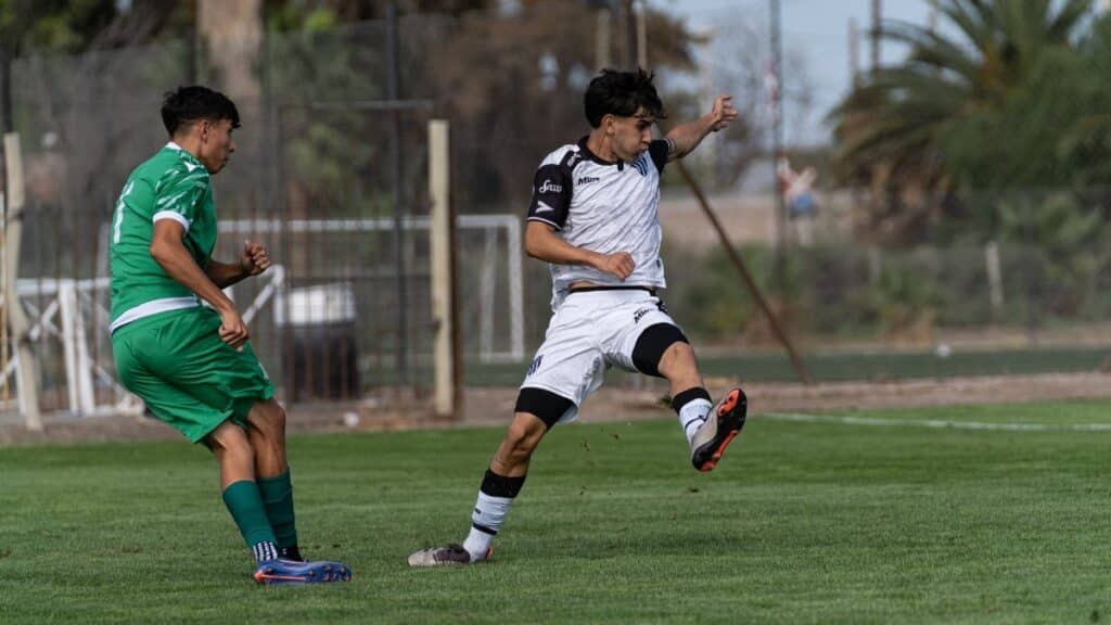 Two soccer players in action during a match, one in green and the other in white uniforms.
