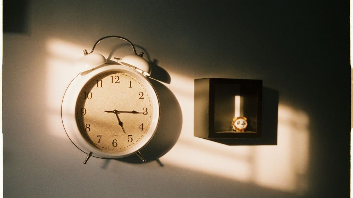 A vintage wall clock illuminated by natural light casting shadows on a wall.