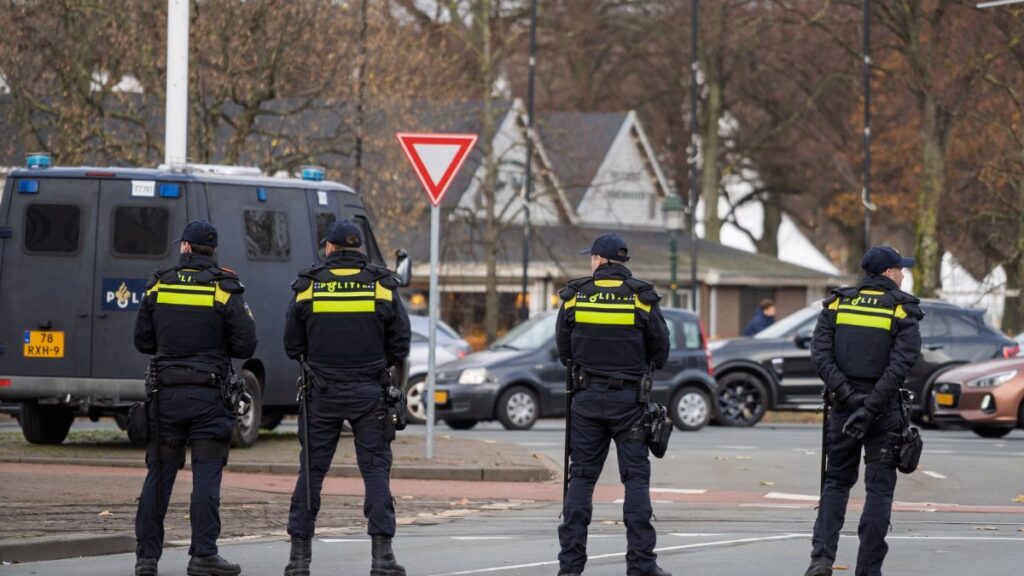 Four police officers stand vigilant on city street near patrol van, ensuring public safety.