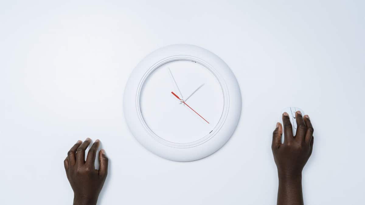 A minimalist image depicting two hands, a wall clock, and a computer mouse on a white surface.