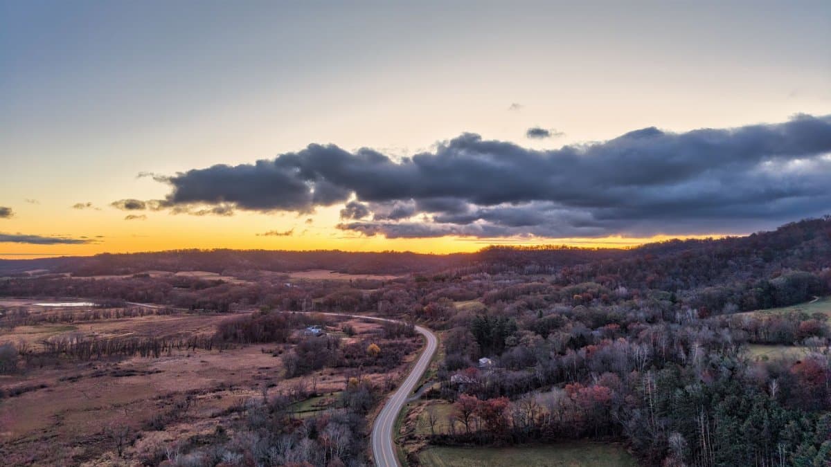 Aerial view of a scenic Wisconsin landscape at sunset with a winding road and autumn foliage.