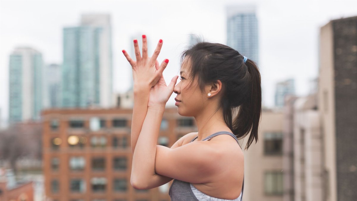 A young woman doing a yoga pose on a rooftop with a city skyline in the background.
