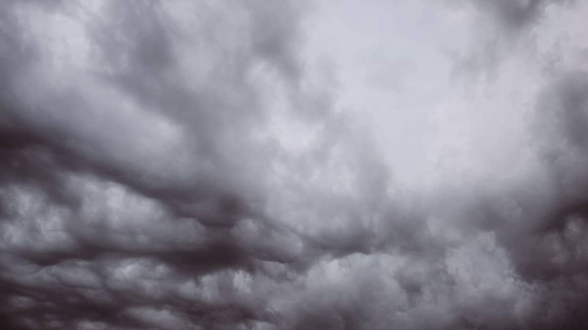 From below black and white view of dramatic overcast skies with dense cumulus clouds in haze