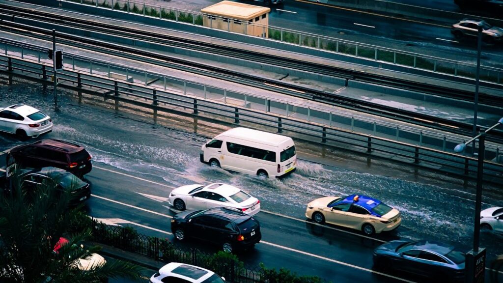 A busy urban street experiencing flooding with vehicles driving through water.