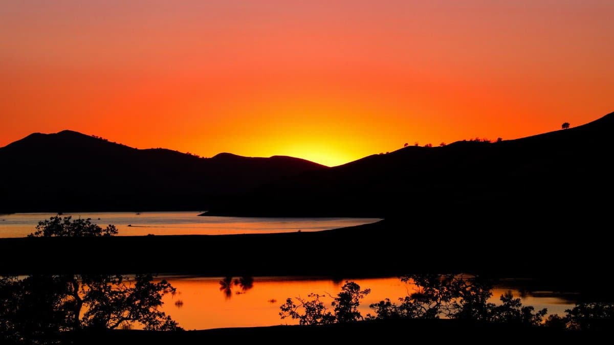 Capture the serene beauty of sunset over lake in Three Rivers, California, with silhouetted hills.