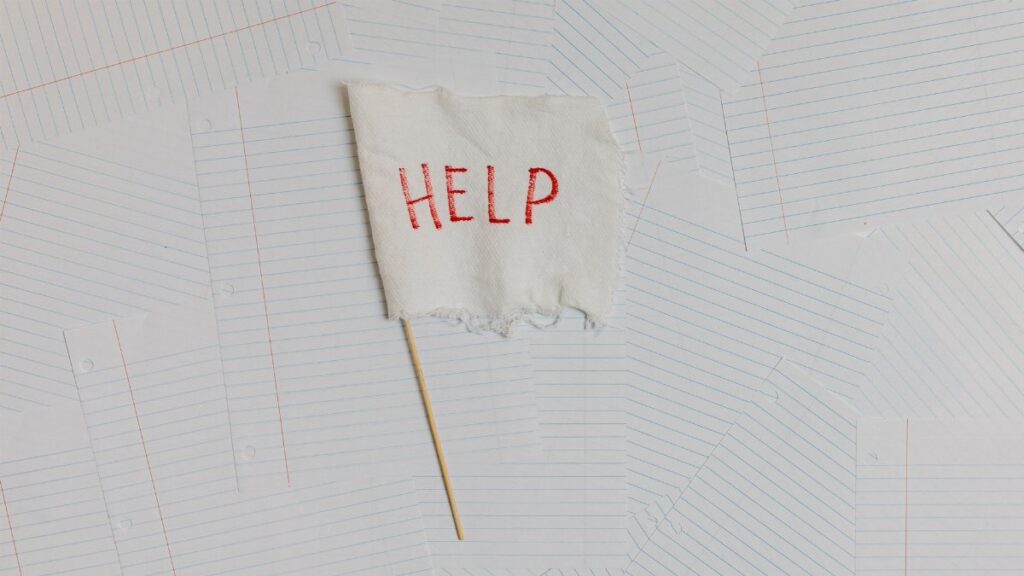 A fabric flag with 'HELP' on a scattered notepaper background, symbolizing distress or overwhelm.