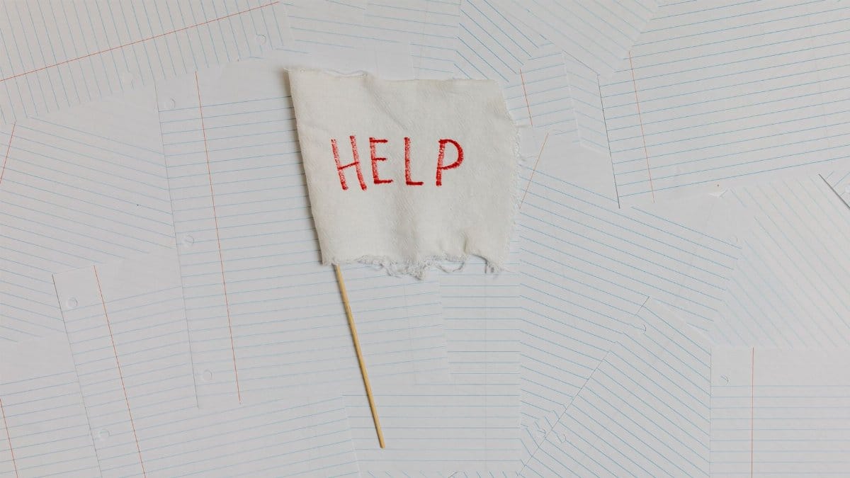 A fabric flag with 'HELP' on a scattered notepaper background, symbolizing distress or overwhelm.