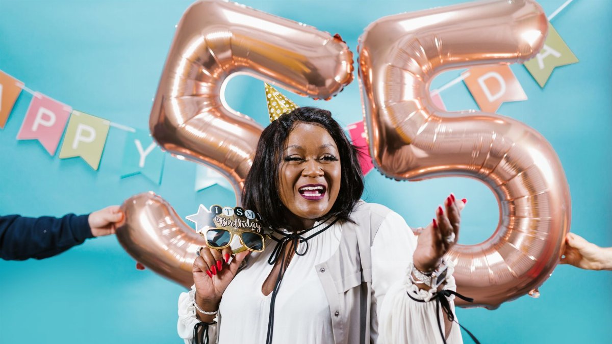 Smiling woman celebrates 55th birthday with balloons and festive decor.